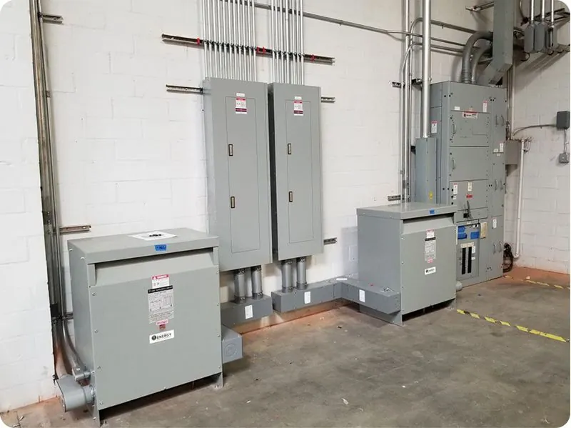 Indoor commercial electrical room with grey panels, disconnects, transformer and conduit