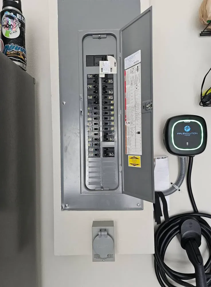 Grey breaker panel with open door next to a wall-mounted EV charger