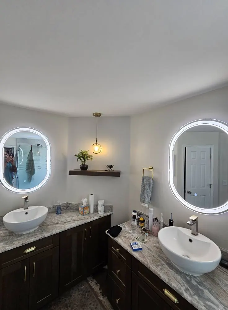 Bathroom vanity with backlit round mirrors and a pendant light